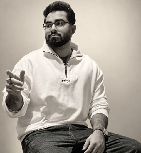 Black and white photo of Surya Sabarwal, seated in a white sweater, pointing toward the camera